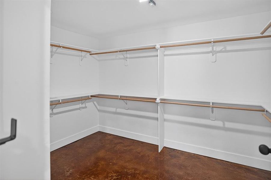 Safe room/ primary walk-in closet featuring an integrated shelving system, multiple hanging rods, white walls, and a dark, textured floor Safe room/ primary walk-in closet featuring an integrated shelving system, multiple hanging rods, white walls, and a dark, textured floor