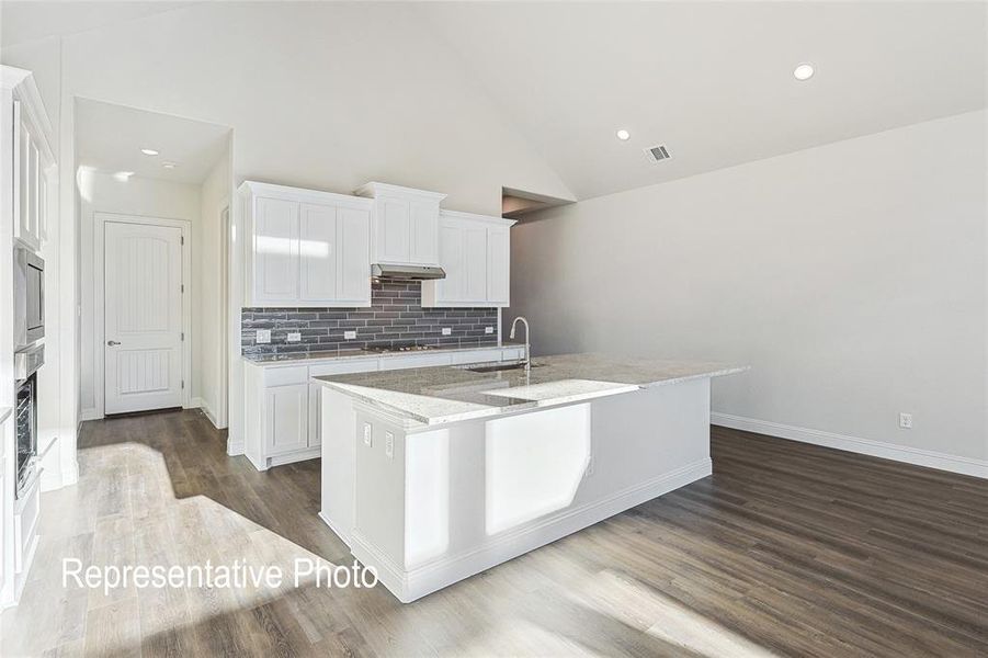 Kitchen featuring high vaulted ceiling, a kitchen island with sink, light stone countertops, and wood-type flooring