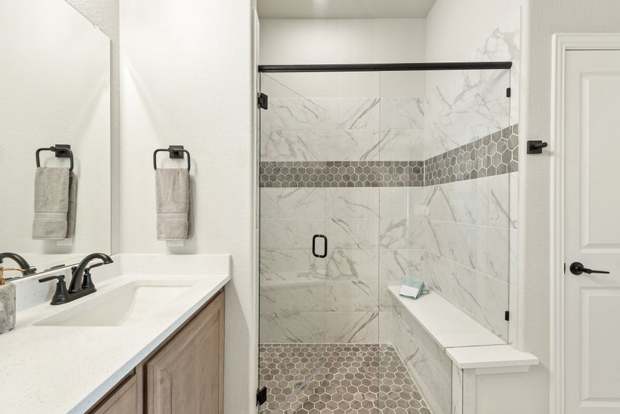 Bathroom with glass walk-in shower featuring marble tile walls, built-in bench, and vanity with white countertop