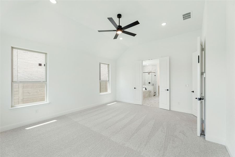 Spacious bedroom with vaulted ceiling, ceiling fan, carpet flooring, and ensuite bathroom doorway Spacious bedroom with vaulted ceiling, ceiling fan, carpet flooring, and ensuite bathroom doorway
