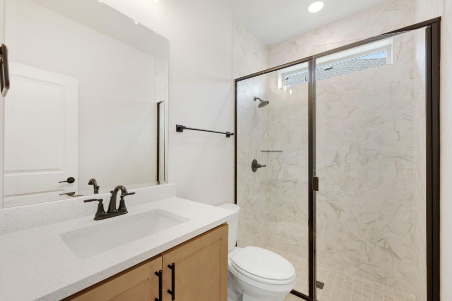 Bathroom with wood vanity, quartz countertop, and glass-enclosed marble tile shower with dark bronze fixtures
