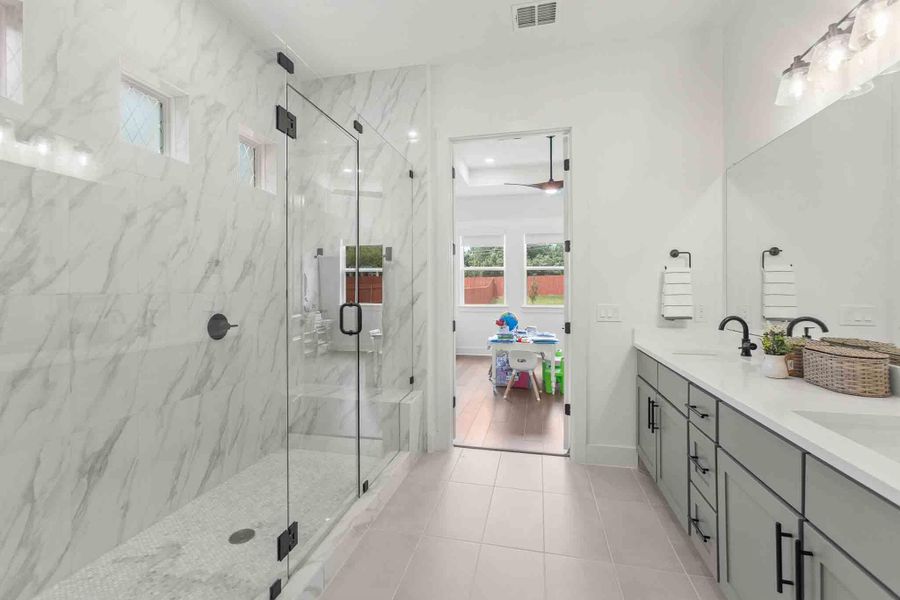 Spacious bathroom featuring a frameless glass shower enclosure with marble-look tile surround and mosaic tile flooring, a dual vanity with light gray cabinetry and black hardware, white countertops, and a large wall-mounted mirror