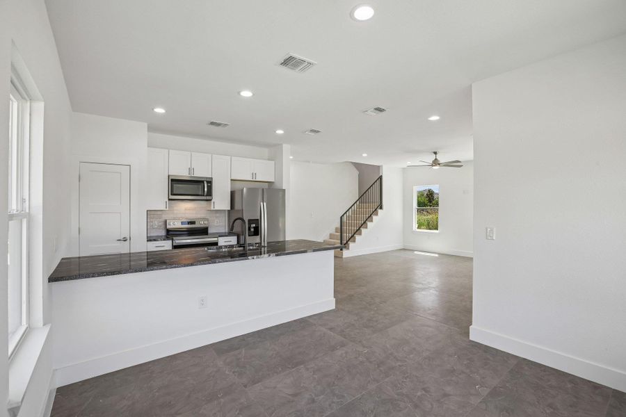 Granite counters highlight a sleek breakfast bar in this open, airy kitchen layout.