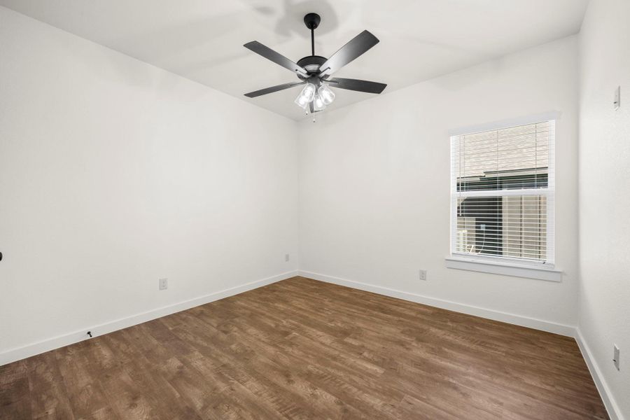 A well-lit bedroom with rich wood flooring and a modern ceiling fan for comfort.