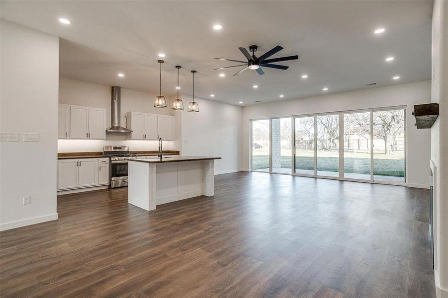 Kitchen featuring white cabinets, ceiling fan, gas stove, a center island with sink, and pendant lighting