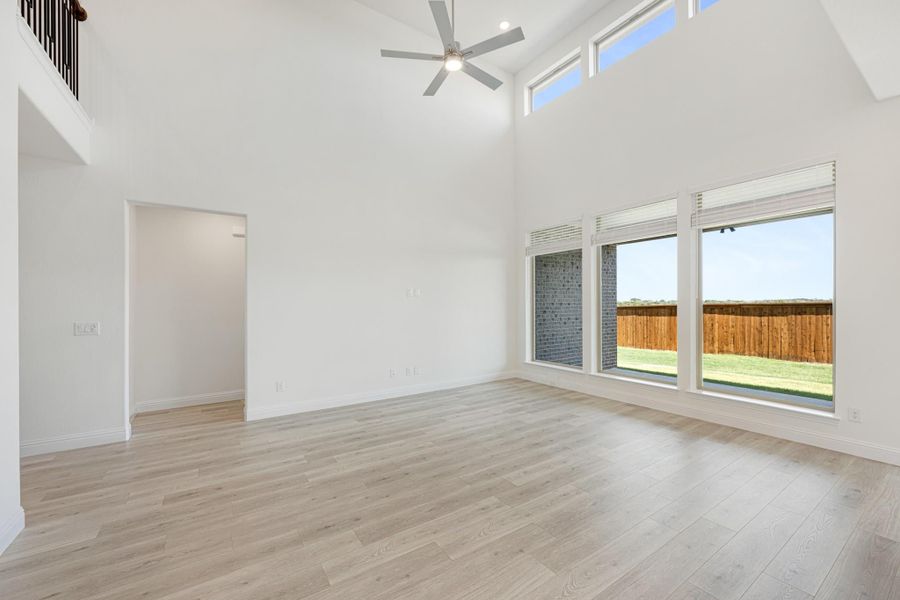 Open living room with vaulted ceiling, ceiling fan, light wood floors, and large windows overlooking backyard Open living room with vaulted ceiling, ceiling fan, light wood floors, and large windows overlooking backyard
