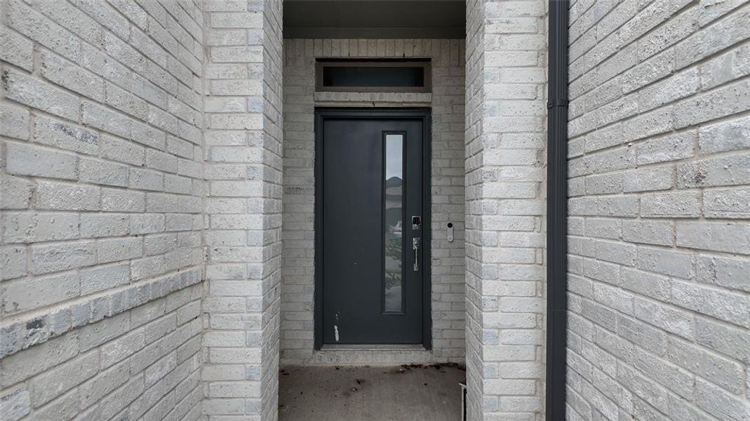 The property features a modern dark grey entry door with a vertical glass insert, set within a light grey brick facade