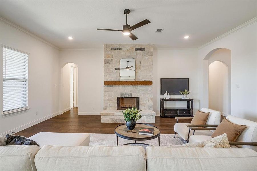 Living room featuring fireplace with stone surround, crown molding, ceiling fan, engineered wood flooring, 10 ft ceilings and 8 ft doors