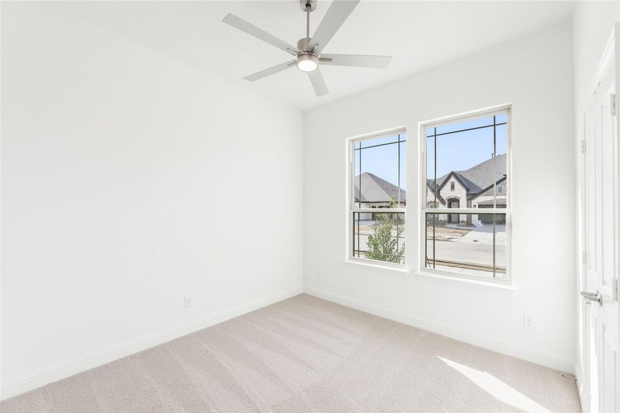Empty bedroom with white walls, carpet flooring, ceiling fan, and two windows overlooking neighborhood homes Empty bedroom with white walls, carpet flooring, ceiling fan, and two windows overlooking neighborhood homes