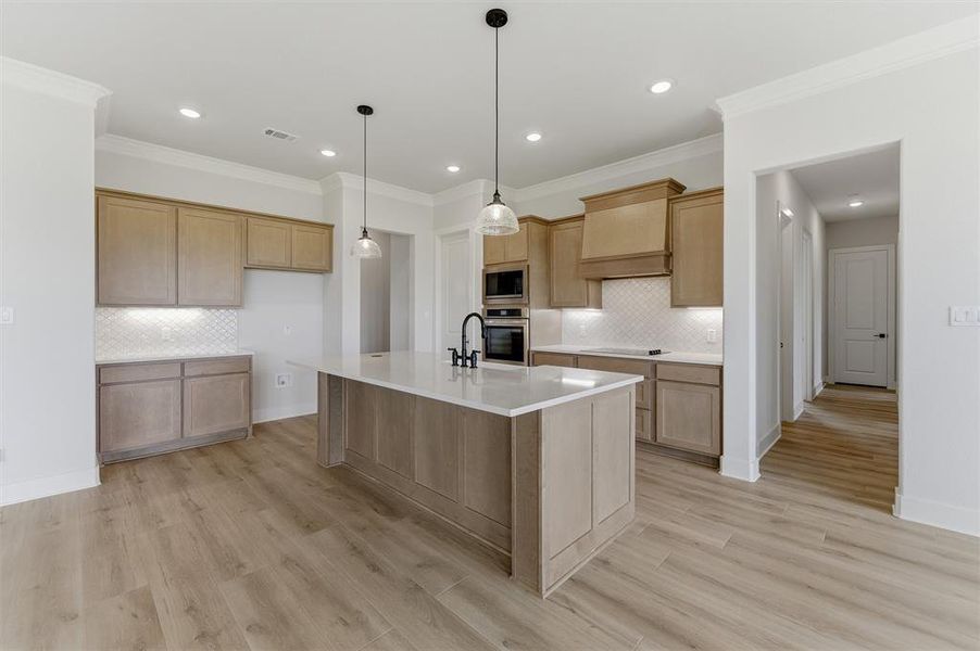 Spacious kitchen featuring a large central island with a white solid surface countertop, light wood-finish cabinetry, built-in double ovens, and a white geometric tile backsplash
