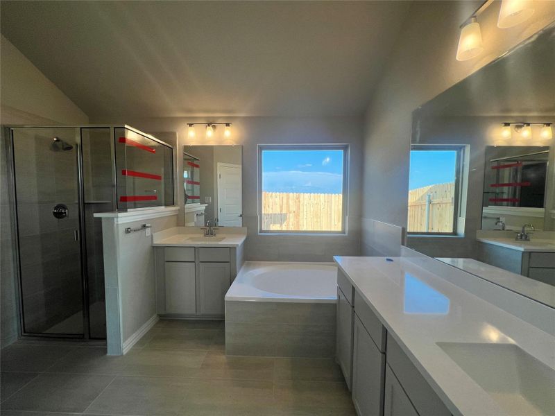 Full bath with vaulted ceiling, a garden tub, a shower stall, two vanities, and light tile patterned floors