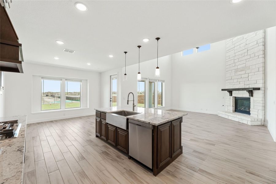 Open kitchen and living area with large island, stone fireplace, high ceilings, and light wood floors Open kitchen and living area with large island, stone fireplace, high ceilings, and light wood floors