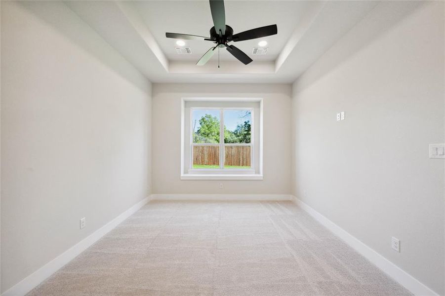 Empty room featuring light colored carpet, a raised ceiling, and ceiling fan