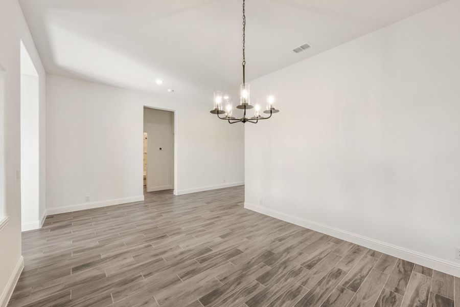 Empty dining room with dark metal chandelier, white walls, and gray wood-look tile floors Empty dining room with dark metal chandelier, white walls, and gray wood-look tile floors