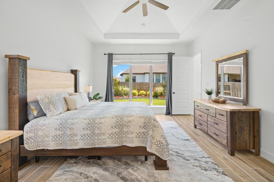 This primary bedroom features, high ceiling with a fan, and abundant natural light from a window overlooking the well-maintained backyard. The room has neutral tones and a cozy atmosphere.