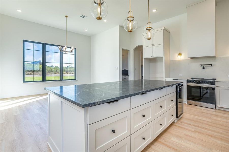 Kitchen featuring white cabinetry, stainless steel range oven, dark stone countertops, decorative light fixtures, and a kitchen island