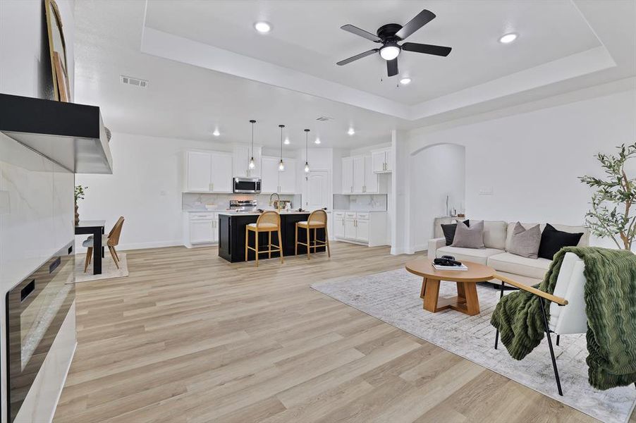 Living room featuring sink, wine cooler, ceiling fan, light wood-type flooring, and a tray ceiling