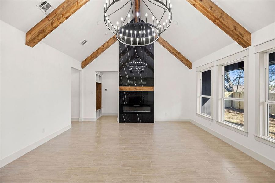 Unfurnished living room with visible vents, a notable chandelier, beamed ceiling, and wood finished floors