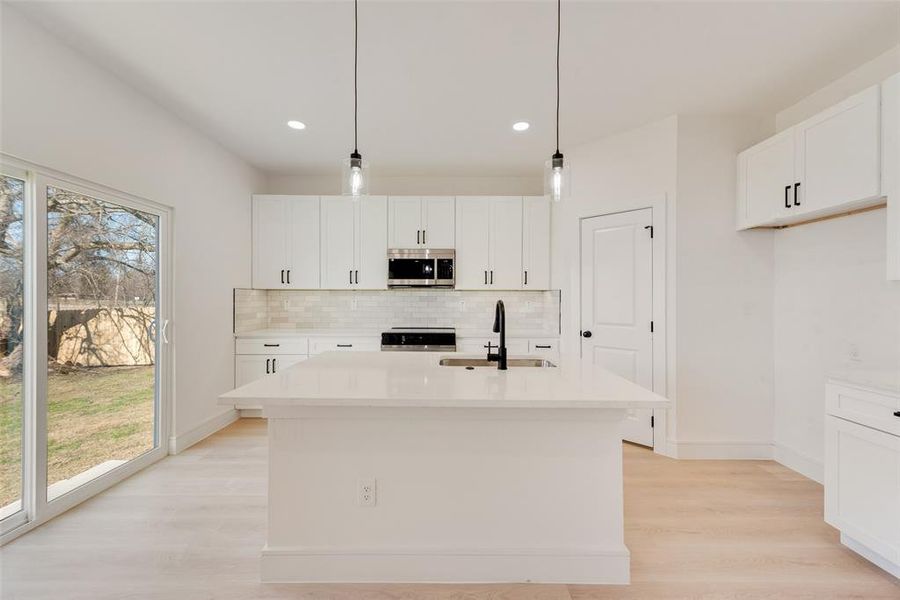 Kitchen with a center island with sink, sink, hanging light fixtures, appliances with stainless steel finishes, and white cabinetry