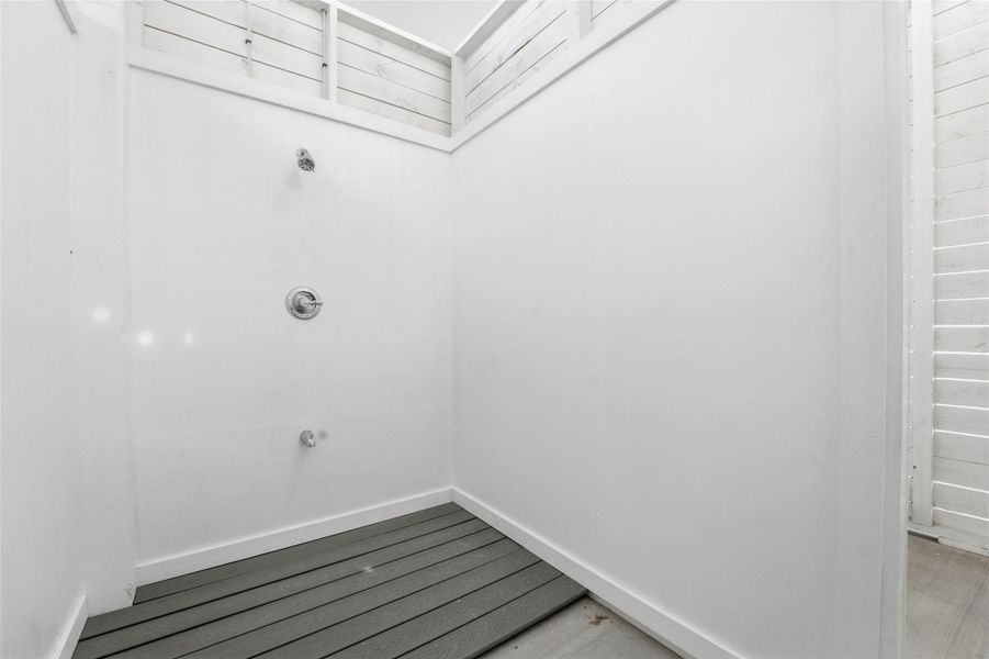 Outdoor shower is located with privacy wall and elevated polywood decking under the home