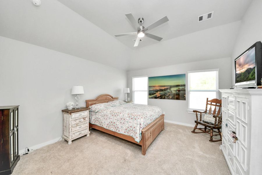 A spacious, peaceful primary suite filled with natural light, featuring soft carpeting and double doors that open to the en-suite bath.