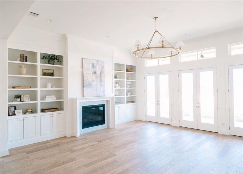 Unfurnished living room with built in shelves, ornamental molding, light hardwood / wood-style flooring, a premium fireplace, and an inviting chandelier