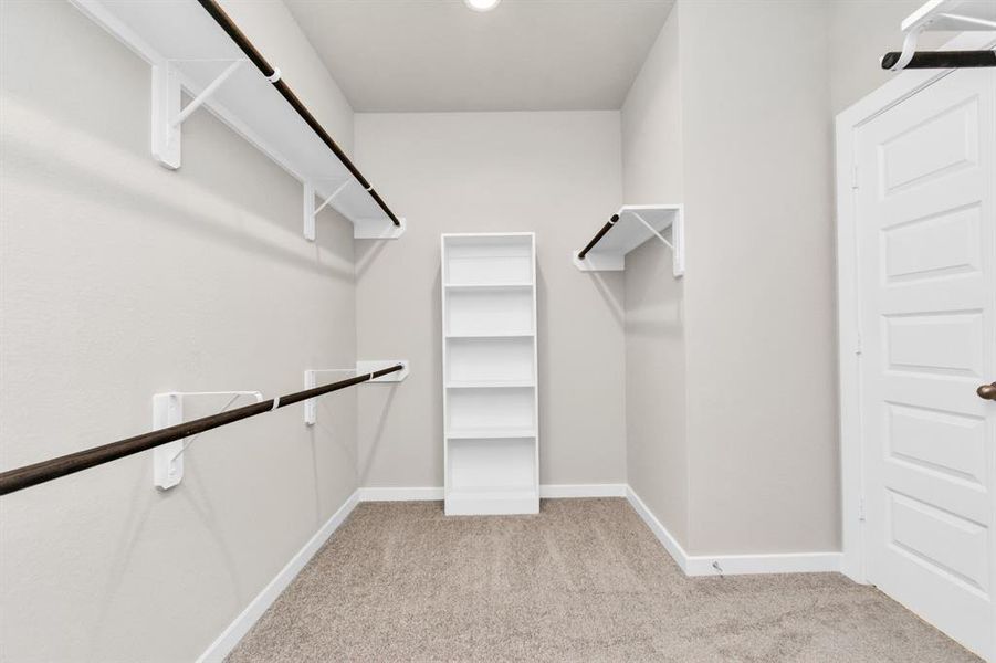 Step into a walk-in closet that defines luxury and functionality. This generously sized space boasts built-in shelving, providing ample room for organization. With high ceilings and recessed lighting, the ambiance is both bright and welcoming. Plush carpeting underfoot enhances the comfort, while warm paint tones add a touch of coziness. Sample photo of completed home with similar floor plan. As-built interior colors and selections may vary.