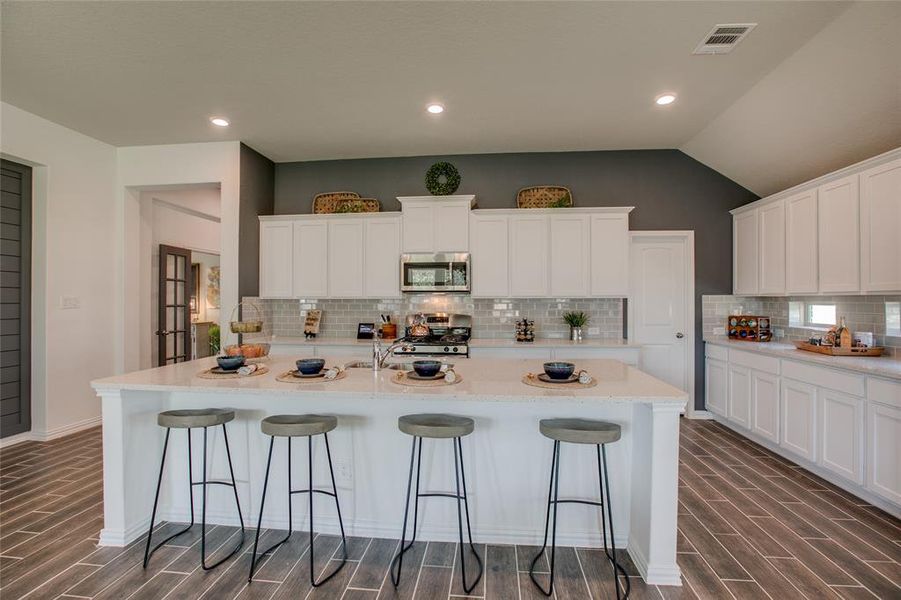 Kitchen featuring tasteful backsplash, wood finish floors, appliances with stainless steel finishes, a kitchen breakfast bar, and lofted ceiling Kitchen featuring tasteful backsplash, wood finish floors, appliances with stainless steel finishes, a kitchen breakfast bar, and lofted ceiling