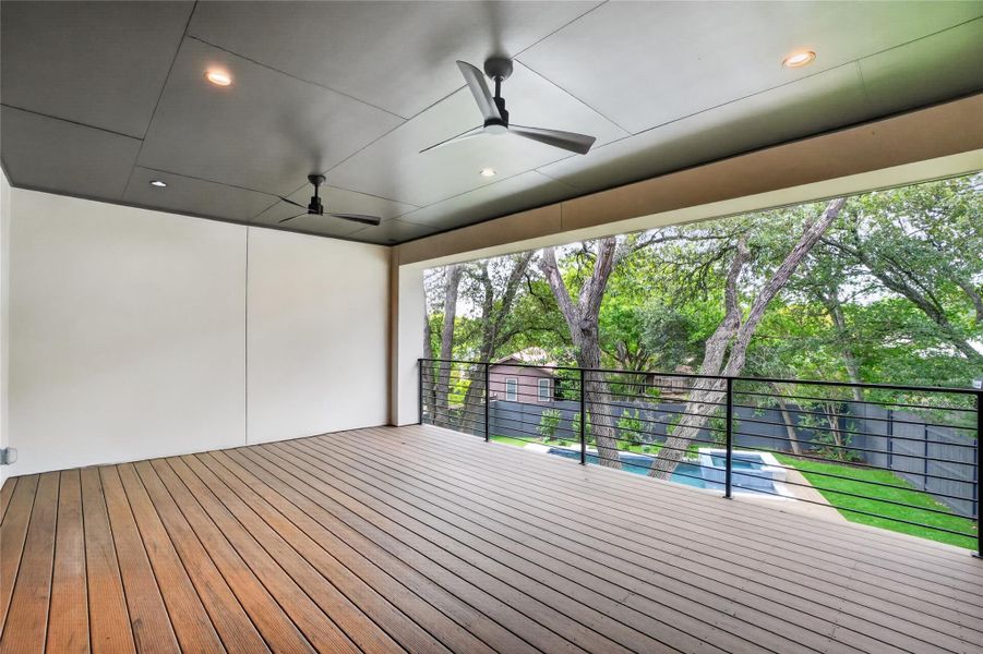 An inviting covered deck with natural wood flooring offers serene views of the surrounding trees and pool.