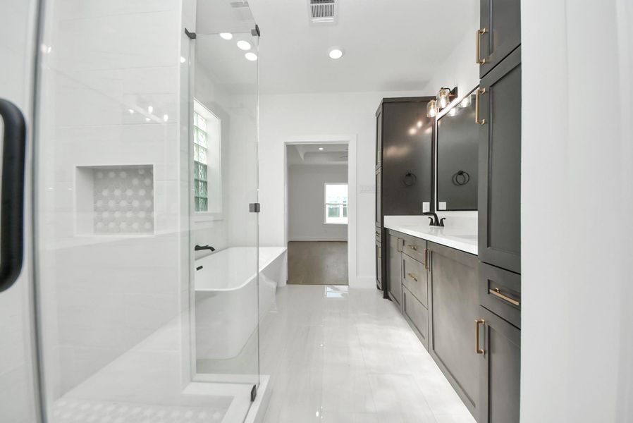 A modern bathroom showcasing dark cabinetry, sleek fixtures, a glass-enclosed shower, and a separate soaking tub. White walls and natural light from a large window create a bright, spa-like atmosphere.