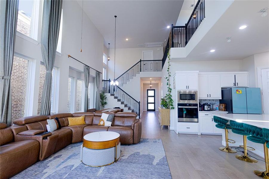 Living room featuring a high ceiling, light wood-style flooring, recessed lighting, and stairway