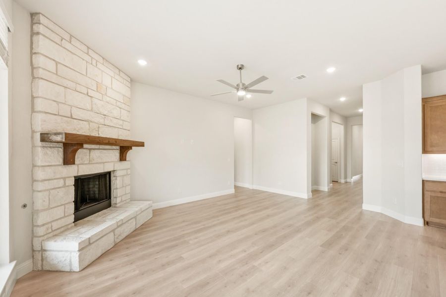 Open living room with floor-to-ceiling stone fireplace, wood mantel, light hardwood floors, and ceiling fan Open living room with floor-to-ceiling stone fireplace, wood mantel, light hardwood floors, and ceiling fan