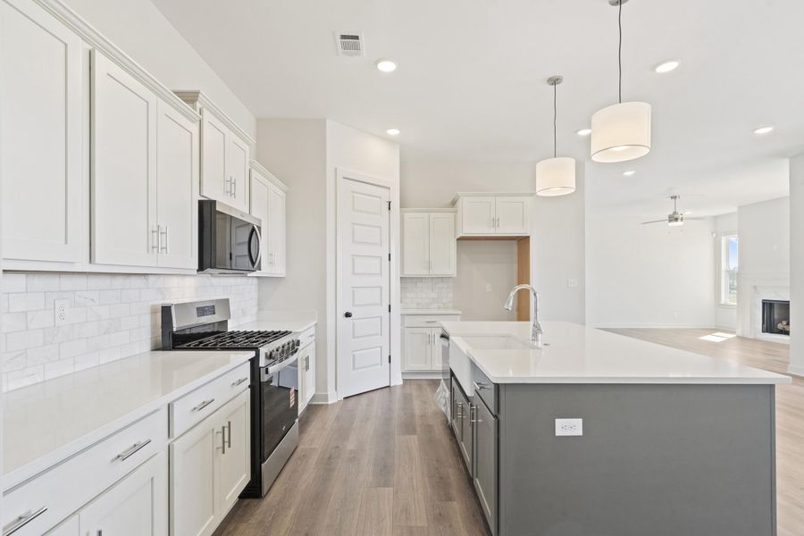 Dual tone kitchen featuring two tone cabinetry, stainless steel appliances, dark wood finished floors, decorative light fixtures, and a fireplace