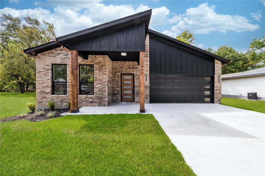 Contemporary home with board and batten siding, a front lawn, driveway, and brick siding