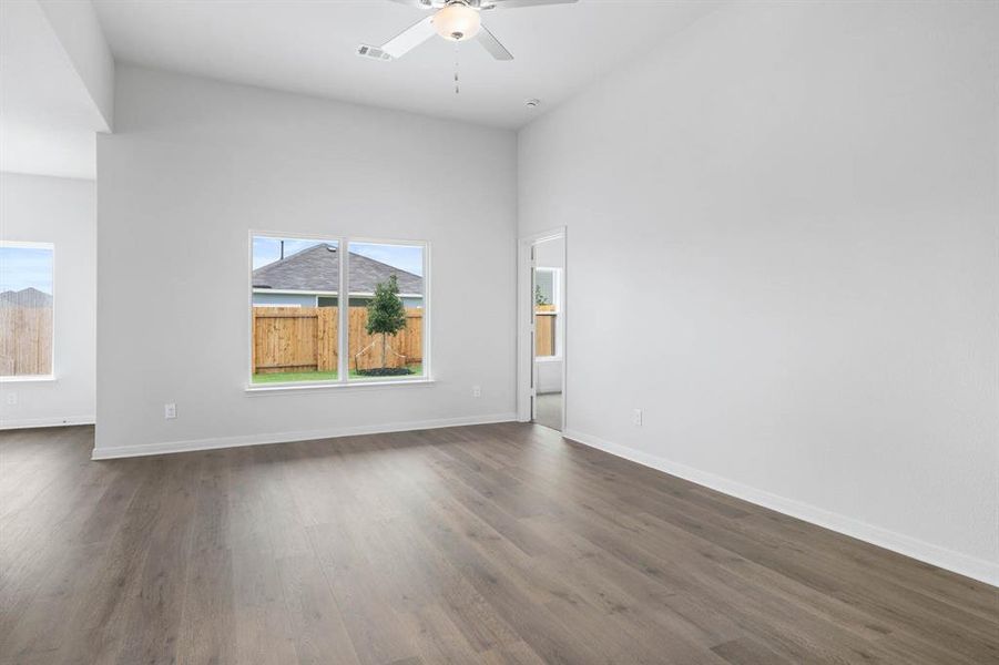Empty room featuring dark wood-type flooring, ceiling fan, and a high ceiling