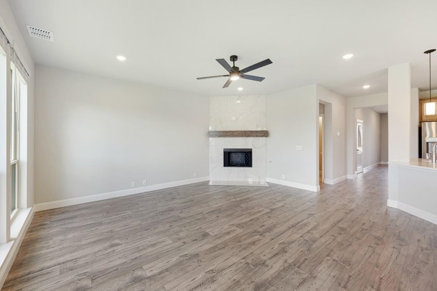 Open living room with hardwood floors, marble fireplace, wood mantel, and ceiling fan