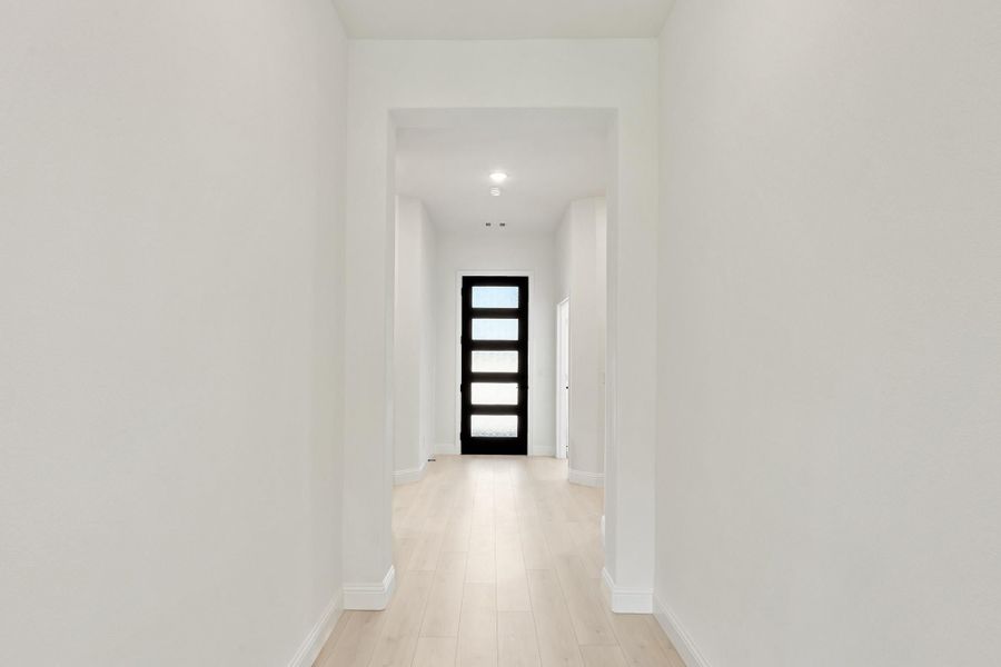 Bright hallway with light wood floors leading to a black front door with glass panels Bright hallway with light wood floors leading to a black front door with glass panels