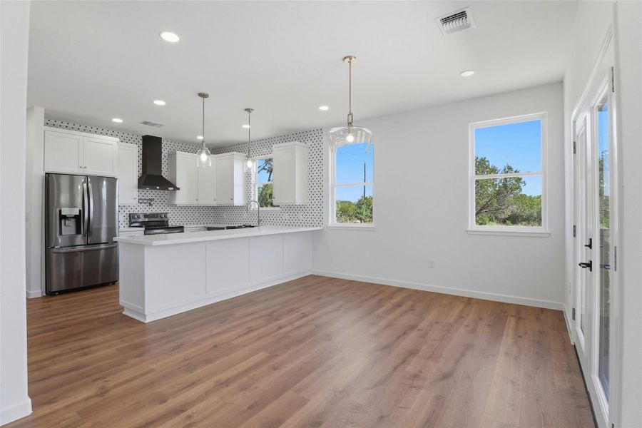 Open-concept kitchen and living area featuring wood-finish flooring, white cabinetry, and stainless steel appliances Open-concept kitchen and living area featuring wood-finish flooring, white cabinetry, and stainless steel appliances