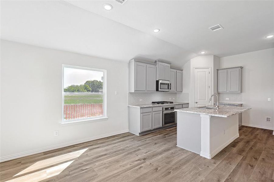 Kitchen with an island with sink, appliances with stainless steel finishes, light wood-type flooring, and gray cabinetry