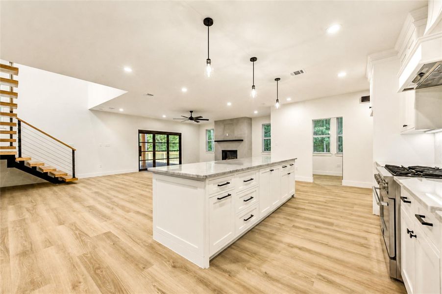 Spacious open-concept living area featuring a modern kitchen with a large island, sleek cabinetry, and stainless steel appliances, complemented by warm LVP flooring and abundant natural light.