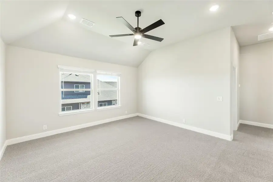 Empty bedroom with vaulted ceiling, ceiling fan, carpet flooring, and two windows Empty bedroom with vaulted ceiling, ceiling fan, carpet flooring, and two windows