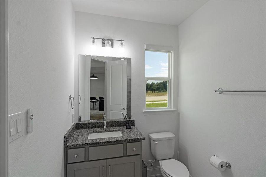 Bathroom featuring a granite-look countertop vanity with gray cabinetry, undermount sink, and a framed mirror