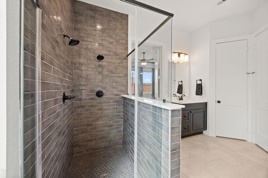 The en-suite bath includes a soaking tub and a spacious glass-enclosed shower with floor-to-ceiling tile and contrasting hex tile flooring.
