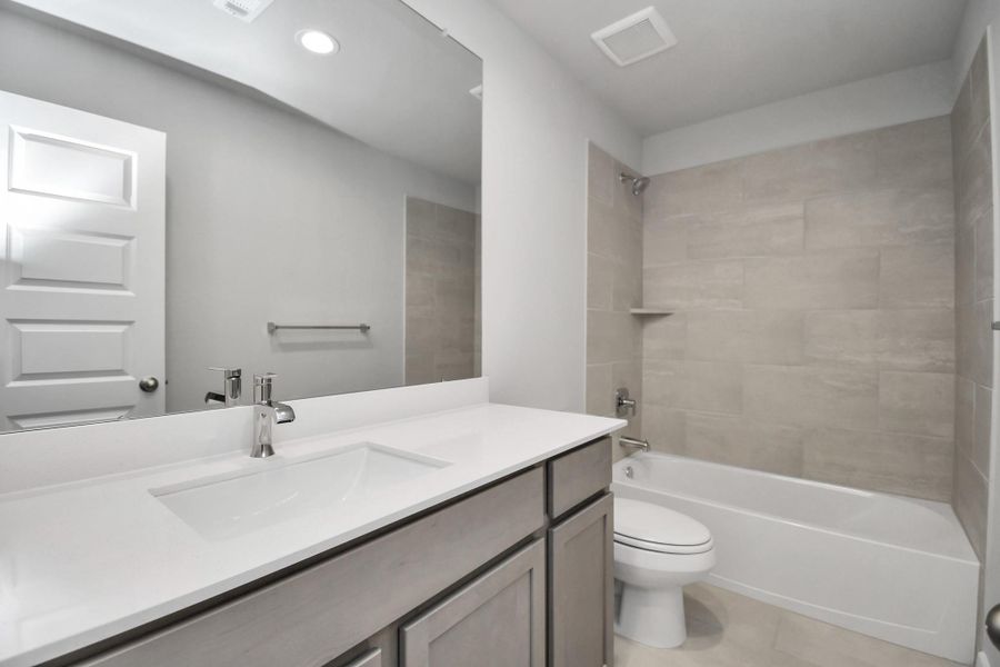 Secondary bath features tile flooring, bath/shower combo with tile surround, light stained wood cabinets, beautiful light countertop.