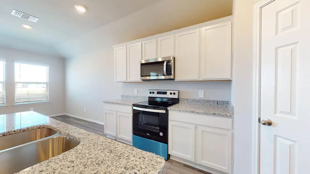 Kitchen featuring stainless steel appliances, white cabinetry, light wood-style flooring, light stone counters, and vaulted ceiling
