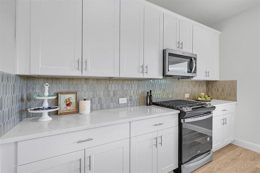 Kitchen featuring appliances with stainless steel finishes, light wood-type flooring, white cabinetry, and backsplash