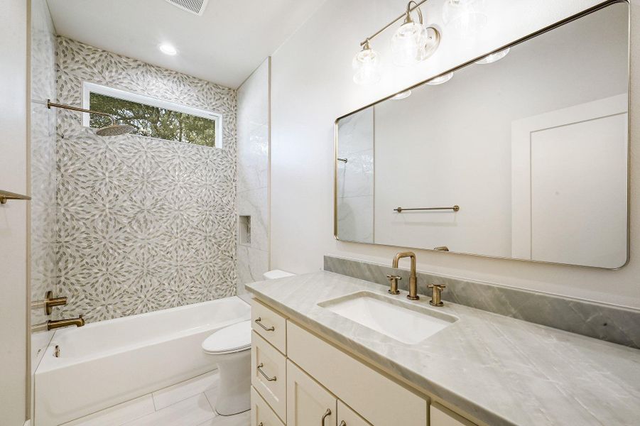 Elegant full bath featuring patterned tile accent wall, brushed gold fixtures, and marble-style counters. Elegant full bath featuring patterned tile accent wall, brushed gold fixtures, and marble-style counters.