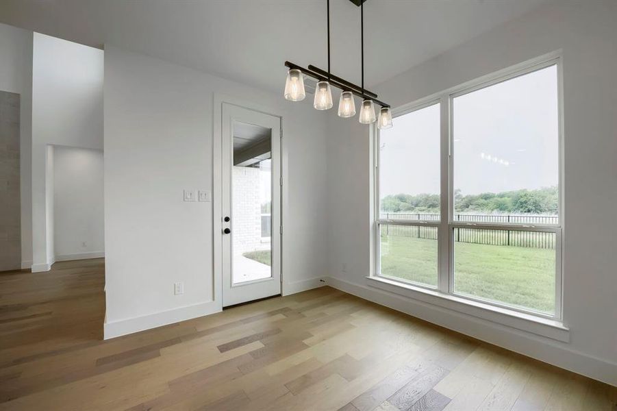 Spacious room featuring wood-finish flooring, a contemporary linear chandelier, and a full-light glass door Spacious room featuring wood-finish flooring, a contemporary linear chandelier, and a full-light glass door