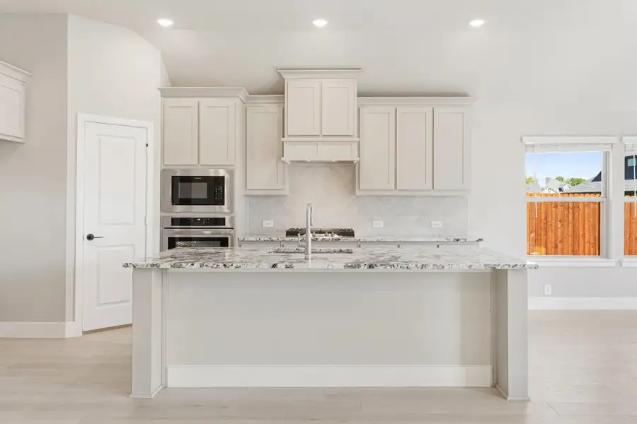Kitchen with large granite island, white cabinets, stainless steel appliances, and tile backsplash