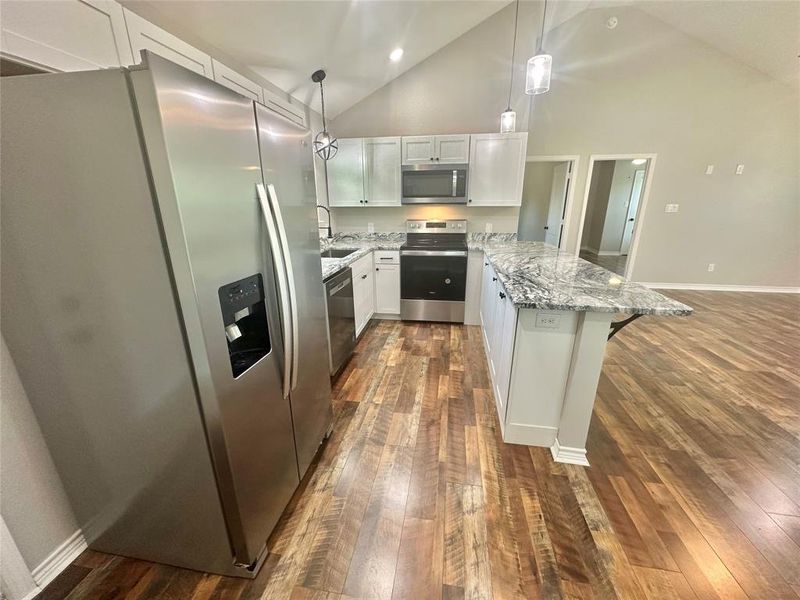 Upstairs Kitchen with appliances with stainless steel finishes, high vaulted ceiling, a peninsula, light stone counters, and LVP floors Upstairs Kitchen with appliances with stainless steel finishes, high vaulted ceiling, a peninsula, light stone counters, and LVP floors
